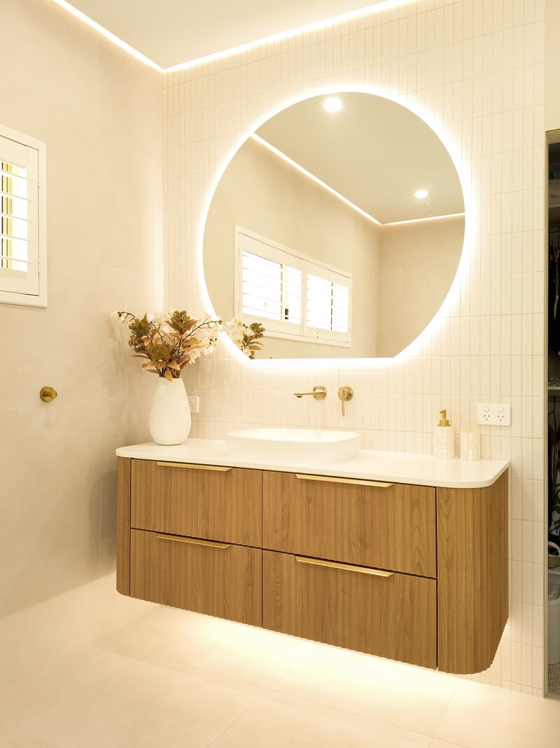 Renovated bathroom with a backlit round mirror, fluted timber vanity and brass tapware