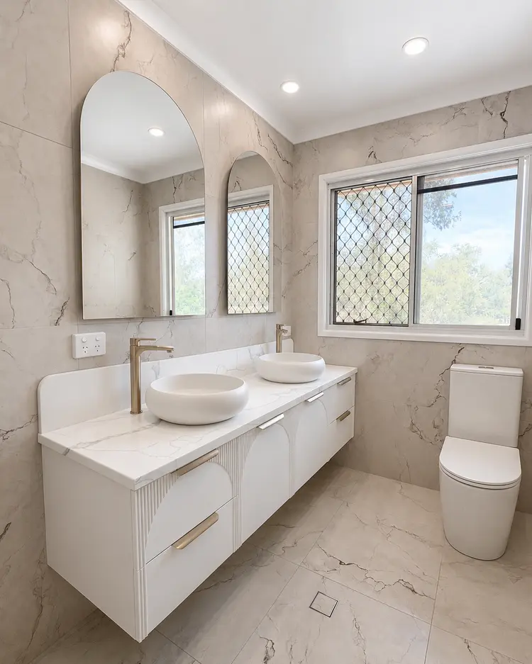 Renovated ensuite with marble-look tiling, double vanity and arched mirrors