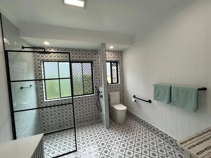 Renovated bathroom with patterned floor tiling, a black-framed shower screen and white panelled walls