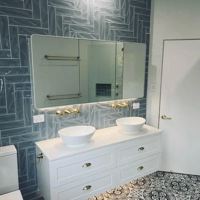 Renovated bathroom with blue herringbone tiling, a double vanity and brass tapware